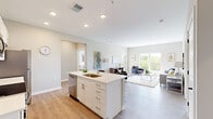 Located at 1179 E Main St in Columbus, Ohio, this well-appointed 2-bedroom, 2-bathroom residence offers a thoughtfully designed open-concept layout. The kitchen serves as the heart of the home, featuring white shaker cabinetry, quartz countertops, stainless steel appliances including a range, microwave, refrigerator, and dishwasher, and a central island with an undermount sink. Light hardwood-style flooring flows seamlessly from the kitchen into the living room, which is bathed in natural light from large windows offering treetop views. A glass door in the living area provides direct access to a private balcony, extending the living space outdoors.

Both bedrooms are carpeted and comfortably sized, with the primary bedroom offering a dedicated walk-in closet lined with shelving and hanging rods. The second bedroom also benefits from natural light and outdoor views via a window overlooking the balcony. Each of the two bathrooms is finished with light cabinetry, quartz countertops, and modern fixtures; one includes a full tub-shower combination. Neutral gray tones throughout the walls complement the bright, contemporary aesthetic, creating a clean and cohesive living environment. A hallway connects all rooms efficiently, completing this functional and modern floor plan.