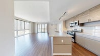 Located at 900 Pacific St in Stamford, Connecticut, this well-appointed 2-bedroom, 2-bathroom residence offers a thoughtfully designed layout across a single floor. Warm hardwood-style flooring flows throughout, complementing the neutral, contemporary palette found in every room.

The open-concept kitchen and living area serves as the heart of the home. The kitchen is equipped with stainless steel appliances — including a gas range, over-the-range microwave, and French door refrigerator — set against a white subway tile backsplash. Textured wood-grain cabinetry extends to the ceiling for ample storage, while a large island with a crisp white quartz countertop and an integrated sink provides additional workspace and casual dining. Track lighting illuminates the space efficiently.

The living room is generously proportioned, featuring floor-to-ceiling sliding glass doors that open to a private balcony, flooding the room with natural light and offering open city views of the Stamford skyline.

Both bedrooms are well-sized, with large windows that continue the theme of natural light and urban views. The spacious primary bedroom is accompanied by a dedicated walk-in closet with built-in wire shelving. The two bathrooms feature modern white floating vanities, backlit mirrors, and wood-look flooring. One bathroom includes a sleek glass-enclosed walk-in shower, while the other offers a bathtub.