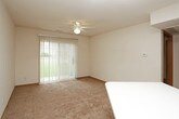 This single-floor unit offers a practical and well-organized layout across several distinct living areas. The living room is a comfortable, open space featuring plush carpeting, a ceiling fan with light fixture, and a large sliding glass door that floods the room with natural light and provides views of a green outdoor area. An adjacent room, also carpeted and bright, benefits from a wide window framing views of surrounding greenery, making it well-suited as a bedroom or flexible living space. A second similarly carpeted room features its own window with natural light, offering a calm and functional environment.

The kitchen is efficiently designed with warm oak cabinetry providing ample storage both above and below the countertops. White appliances, including a range and oven, complement the light-colored countertops, while a stainless steel sink sits beneath upper cabinets. Light tile flooring completes the clean, functional aesthetic.

Two full bathrooms serve the unit, each featuring a tub-shower combination, toilet, and a vanity with wood cabinetry. Both bathrooms are finished with tile flooring and maintain a clean, neutral palette. Throughout the unit, neutral wall tones and consistent wood-trimmed baseboards create a cohesive and understated ambiance.