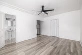 This 230 square foot studio apartment in Los Angeles offers a thoughtful blend of compact living and modern design. The space is efficiently laid out on a single floor, comprising a living room, kitchen, and bathroom. The living area features light-toned wood-look flooring that extends throughout, creating a sense of continuity and spaciousness. A modern ceiling fan with sleek blades adds both style and functionality.

The kitchen, though compact, is well-equipped with white cabinetry, providing ample storage. It includes a stainless steel refrigerator and a dark countertop, creating a striking contrast against the white cabinets. A sink with a modern black faucet completes the functional space.

The bathroom, while not expansive, offers essential amenities including a shower with a black showerhead, maintaining the contemporary aesthetic found throughout the apartment. The overall color scheme of whites and light neutrals contributes to a bright, airy feel despite the limited square footage.

Crown molding adds a touch of elegance to the space, while the minimalist design approach maximizes the available area. This studio apartment represents an ideal solution for those seeking efficient, low-maintenance urban living in the heart of Los Angeles.