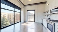 This single-floor industrial loft masterfully blends raw architectural character with modern finishes. Polished concrete floors run throughout the entire space, reflecting natural light and anchoring the open, airy layout. Whitewashed exposed brick walls and soaring ceilings with visible metal ductwork and steel beams pay homage to the building's industrial heritage, creating a striking backdrop for contemporary living.

The open living area is bathed in natural light courtesy of oversized black-framed windows that frame views of the surrounding urban streetscape. The kitchen is thoughtfully designed with white cabinetry, white subway tile backsplash, open wooden shelving, and a full suite of stainless steel appliances including a gas range, dishwasher, over-range microwave, and a large refrigerator.

The bedroom area features generous built-in closet storage with shelving and hanging space, accessed through a sliding panel door. The bathroom is outfitted with a walk-in shower clad in vertical white tile, a wood-toned vanity with a white undermount sink, and a medicine cabinet mirror. A separate half bath provides additional convenience. Throughout, the design balances utilitarian industrial elements with clean, modern aesthetics for a cohesive and sophisticated urban living experience.
