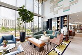 Located at 14020 Stream Way in Charlotte, NC, this sophisticated single-floor living space offers a generously proportioned communal lounge designed with a bold, contemporary aesthetic. The space is anchored by dramatic double-height ceilings that amplify the sense of openness, while expansive floor-to-ceiling windows flood the interior with natural light and frame views of the outdoor terrace and surrounding community.

The living area is thoughtfully divided into distinct seating zones, each curated with eclectic, design-forward furnishings. A curved sage-green sectional sofa, patterned armchairs, and layered geometric rugs create a warm yet vibrant atmosphere. Striking teal and neutral wall art panels punctuate the soaring white walls above, adding an artistic focal point.

A sleek built-in fireplace clad in metallic tile serves as a dramatic feature wall, paired with a mounted flat-screen display and flanked by floor-to-ceiling wood-paneled doors that open directly to the outdoor pool area. Opposite, a fully appointed wet bar with brass-accented cabinetry, mirrored shelving, and counter seating provides an elegant entertaining hub.

Rich wood-paneled walls, built-in bookshelves with curated décor, herringbone hardwood flooring, and a bold checkered tile inset contribute to the space's layered, upscale character. The overall ambiance is lively yet refined, blending comfort with high-design sensibility.