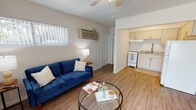This single-story residence in Gainesville, Florida offers a thoughtfully arranged floor plan that connects the living, kitchen, and bedroom areas in a clean, functional layout. The living room serves as the central gathering space, featuring light wood-style flooring, a ceiling fan, and multiple windows dressed with vertical blinds that allow natural light to filter in. A sliding glass door opens to the outdoors, enhancing the sense of openness. A wall-mounted air conditioning unit provides climate control throughout the space.

The kitchen is positioned adjacent to the living area and is equipped with light wood cabinetry, light-toned quartz-style countertops, an undermount stainless steel sink with a brushed nickel faucet, a white electric range, and a full-size refrigerator. A range hood is installed above the cooktop, and ample upper cabinet storage keeps the space organized.

The bedroom is a well-proportioned room with wood-style flooring, a ceiling fan, and a window providing natural light. Built-in open shelving along one wall adds practical storage. The bedroom connects directly to a private bathroom featuring white subway-style tile wainscoting, a vanity with under-sink cabinet storage, a framed mirror, and a shower with curtain enclosure.