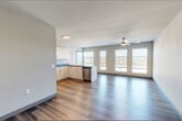 This well-appointed 2-bedroom, 1-bathroom single-floor residence offers a thoughtfully designed layout with modern finishes throughout. The open-concept kitchen and living area serves as the heart of the unit, featuring light wood cabinetry, dark countertops, a peninsula with an integrated sink, stainless steel appliances including a refrigerator, range, and dishwasher, and pendant lighting overhead. A ceiling fan and a bank of large windows flood the living area with natural light while providing views of the surrounding neighborhood. Durable wood-style plank flooring extends throughout the main living spaces, adding warmth and continuity to the design. The primary bedroom is a comfortable and well-proportioned space with carpet flooring, a ceiling fan, a closet with built-in shelving, and a window with outdoor views. The second bedroom also features carpet flooring, a ceiling fan, and windows that bring in natural light. The bathroom is finished with a single vanity with a white countertop, a large mirror, and wood-style flooring. A dedicated laundry area provides the convenience of an in-unit washer and dryer. A hallway connects all rooms, contributing to the unit's efficient and functional floor plan.