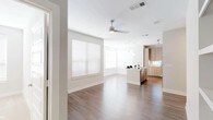 This well-appointed single-floor residence showcases a contemporary design with a neutral color palette and quality finishes throughout. The open-concept living area features rich hardwood-style flooring, a ceiling fan, and generous windows dressed with horizontal blinds that invite abundant natural light into the space.

The kitchen is a standout feature, equipped with warm wood-toned cabinetry extending to the ceiling for ample storage, stone-look countertops, a white tile backsplash, and a full suite of stainless steel appliances including a range, microwave, and refrigerator. A central island with an undermount sink and pendant lighting adds both functionality and style to the space.

The bedroom is generously sized with plush carpeting, a ceiling fan, and multiple windows that flood the room with natural light. An expansive walk-in closet connects to the bedroom, offering a well-designed built-in system with double hanging rods, open shelving, and dedicated storage cubbies.

Two bathrooms serve the residence. The primary bathroom features a long double-sink vanity with stone countertops, light wood cabinetry, bright lighting, and a glass-enclosed walk-in shower with elegant tile surround. The secondary bathroom mirrors the same refined aesthetic with a frameless glass shower enclosure, stone-topped vanity, and wood-finish upper cabinetry. Together, these spaces create a cohesive, modern living environment.