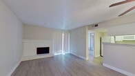 This single-floor residence offers a well-organized layout with consistent finishes throughout, highlighted by light-toned laminate wood flooring that flows seamlessly from room to room. The living area serves as the heart of the home, anchored by a white brick fireplace and large sliding glass door dressed with vertical blinds that invite generous natural light into the space. Neutral gray walls and a textured ceiling complement the clean, understated aesthetic.

The kitchen is outfitted with white cabinetry extending to the ceiling for ample storage, light stone-look countertops, and a full suite of white appliances including a refrigerator, electric range, and over-the-range microwave. A skylight above adds a bright, open quality to the cooking space, and a pass-through counter connects it to an adjacent dining or flex area.

The bedroom is generously proportioned, featuring a ceiling fan, a sliding glass door for additional natural light, and a wall of mirrored sliding closet doors paired with open built-in shelving for organized storage. The bathroom presents a long vanity with white cabinetry and stone-look counters, a mirror, and a separate tub-shower combination. Ceiling fans are present in multiple rooms, and the overall design reflects a clean, move-in ready condition throughout.