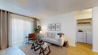 Located at 8120 E 63rd Pl in Tulsa, Oklahoma, this single-floor unit offers a well-organized and comfortable layout with a warm, modern aesthetic throughout. The living room serves as the heart of the space, featuring wood-look flooring, a textured ceiling, and a large sliding glass door with vertical blinds that floods the room with natural light and provides access to the outdoors. The kitchen is a functional galley-style space equipped with wood-toned cabinetry, white countertops, a stainless steel sink, and black appliances including a refrigerator and range. Adjacent to the kitchen is a cozy dining nook with enough room for an intimate table setting, accented by neutral walls and additional natural light. The unit includes two bedrooms, each with distinct character. The primary bedroom features a bold dark accent wall, warm ambient lighting, and wood-look flooring, creating a restful retreat. The second bedroom is bright and airy, with a large window dressed in sheer curtains that allow soft natural light to fill the space. The full bathroom is clean and classic, offering a vanity with wood cabinetry, a wide mirror, and a tub-shower combination with tile surround. The overall ambiance is light, neutral, and inviting throughout.
