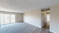 This single-floor residence offers a well-organized layout designed for comfortable everyday living. The living area serves as the heart of the space, featuring plush gray carpeting that transitions to wood-look vinyl plank flooring along its border. Neutral-toned walls and a textured ceiling create a clean, understated backdrop, while a large sliding glass door floods the room with natural light and provides direct access to an outdoor balcony.

The galley-style kitchen is efficiently arranged with rich mahogany cabinetry lining both sides, granite-look countertops, a stainless steel sink, and black appliances including a refrigerator and electric range. Light wood-look flooring runs through this area, complementing the warm cabinetry tones.

Multiple bedrooms are finished with wall-to-wall carpeting in neutral tones, each featuring windows fitted with horizontal blinds that allow natural light while maintaining privacy. At least one bedroom includes a built-in closet with bifold doors, adding practical storage. The bathroom features a full-size soaking tub with an overhead shower and clean white surround panels. Throughout the space, consistent neutral paint tones, white trim, and textured ceilings create a cohesive, move-in-ready ambiance.