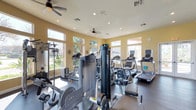 The fitness center at 1390 Santa Alicia in Chula Vista is a well-appointed, single-floor exercise facility designed to support a comprehensive workout experience. The space is bathed in natural light, thanks to large windows lining multiple walls that offer views of lush outdoor greenery, creating an energizing and open atmosphere. Recessed lighting and dual ceiling fans ensure the room remains well-lit and comfortably ventilated throughout the day. The fitness floor is generously equipped with a variety of cardio machines, including multiple treadmills and stationary bikes, providing ample options for aerobic training. A multi-station cable and weight machine anchors the strength-training section, offering versatile resistance exercises for users of varying fitness levels. The equipment is thoughtfully arranged to allow ease of movement and safe use throughout the space. The warm yellow-toned walls and durable flooring contribute to a clean, welcoming environment. Whether focused on cardio endurance, strength building, or general fitness, this facility provides residents with a convenient and fully equipped space to meet their health and wellness goals.