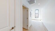 This single-floor space is designed with a clean, modern aesthetic throughout, characterized by crisp white walls, light wood-style flooring, and an open, airy feel. The layout connects the primary living area, kitchen, and bathroom in a cohesive flow that maximizes the available square footage.

The living area is a standout feature, anchored by three tall, arched windows with dark metal frames that flood the room with natural light and offer views of the surrounding urban streetscape. Sunlight casts bright patterns across the light-toned floors, enhancing the spacious and welcoming atmosphere.

The kitchen is well-appointed with white shaker-style cabinetry extending to the ceiling for generous storage, complemented by warm-toned countertops. A full suite of stainless steel appliances includes a refrigerator, gas range, over-the-range microwave, and dishwasher, providing a functional and stylish cooking environment.

The bathroom features a combined tub and shower, a white vanity with an undermount sink set in a warm-toned countertop, and a large mirror. Finishes include brushed gold hardware, adding a refined touch.

A hallway connects the rooms efficiently, with ceiling-mounted HVAC and recessed lighting providing year-round climate control and consistent illumination throughout the unit.