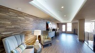 This single-floor space makes a strong first impression with its thoughtfully curated design elements and welcoming ambiance. The most commanding feature is a floor-to-ceiling textured wood-panel accent wall, composed of layered horizontal strips in varying natural tones, adding warmth and visual depth to the interior. Recessed lighting is strategically placed throughout the tray ceiling, casting a soft, even glow that complements the clean white ceiling finish.

The space is furnished with contemporary wingback chairs in neutral upholstery, accented by colorful throw pillows that introduce subtle pops of color. A geometric concrete side table and a classic white table lamp contribute to the modern yet approachable aesthetic. A low-profile dresser-style console serves as a display surface, styled with decorative objects and a table lamp.

Smooth, light-toned hardwood flooring runs throughout, unifying the space and enhancing its sense of openness. Natural light filters in through glass-paneled double doors at the far end, offering a view to the exterior and brightening the room. Overall, the space balances modern design with comfortable, inviting details.