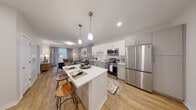 This thoughtfully designed single-floor residence offers a seamless blend of modern aesthetics and functional living. The open-concept layout connects the kitchen and living area, creating a bright and inviting atmosphere. The kitchen is a standout feature, equipped with stainless steel appliances including a French door refrigerator, electric range, built-in microwave, and dishwasher. White shaker-style cabinetry pairs with a classic subway tile backsplash and crisp white countertops, while a central island with seating provides additional prep space and casual dining. Pendant lighting overhead adds a warm, polished touch. The living area extends naturally from the kitchen, featuring warm hardwood-style flooring, a neutral gray accent wall, and sliding glass doors that open to an outdoor balcony, filling the space with natural light. The bedroom offers plush carpeting, a large window with outdoor views, and a calm, restful ambiance enhanced by soft neutral tones. The bathroom is finished with large-format light tile flooring, a vanity with ample storage, and clean white paneled doors. Throughout the residence, a cohesive contemporary design palette ties each space together, creating a comfortable and refined living environment.
