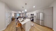 This thoughtfully designed single-floor residence offers a seamless blend of modern aesthetics and functional living. The open-concept layout connects the kitchen and living area, creating a bright and inviting atmosphere. The kitchen is a standout feature, equipped with stainless steel appliances including a French door refrigerator, electric range, built-in microwave, and dishwasher. White shaker-style cabinetry pairs with a classic subway tile backsplash and crisp white countertops, while a central island with seating provides additional prep space and casual dining. Pendant lighting overhead adds a warm, polished touch. The living area extends naturally from the kitchen, featuring warm hardwood-style flooring, a neutral gray accent wall, and sliding glass doors that open to an outdoor balcony, filling the space with natural light. The bedroom offers plush carpeting, a large window with outdoor views, and a calm, restful ambiance enhanced by soft neutral tones. The bathroom is finished with large-format light tile flooring, a vanity with ample storage, and clean white paneled doors. Throughout the residence, a cohesive contemporary design palette ties each space together, creating a comfortable and refined living environment.