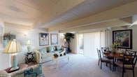This two-bedroom, one-and-a-half-bath townhouse is spread across two floors, offering a well-organized layout with distinct living and sleeping areas. The main level centers around a spacious living and dining area characterized by exposed ceiling beams and white-painted brick accent walls that lend a rustic yet refined architectural character. Soft carpeting runs throughout the living space, contributing to a warm, comfortable ambiance. A large sliding glass door floods the room with natural light and provides direct access to an outdoor patio area, making the living space feel open and connected to the exterior.

Adjacent to the living area, the kitchen is efficiently designed with light wood cabinetry, a double stainless steel sink, electric range with built-in microwave, and a pass-through window that maintains visual connectivity with the living room. Hardwood-style flooring grounds the kitchen in a practical, easy-to-maintain finish.

The two bedrooms, located on the upper level, each feature the same exposed beam detailing and white brick accent walls seen throughout the home. Both rooms are carpeted and offer ample space for furnishings. The full bathroom includes a tub-shower combination with tile flooring, while a half-bath provides added convenience for guests on the main level.