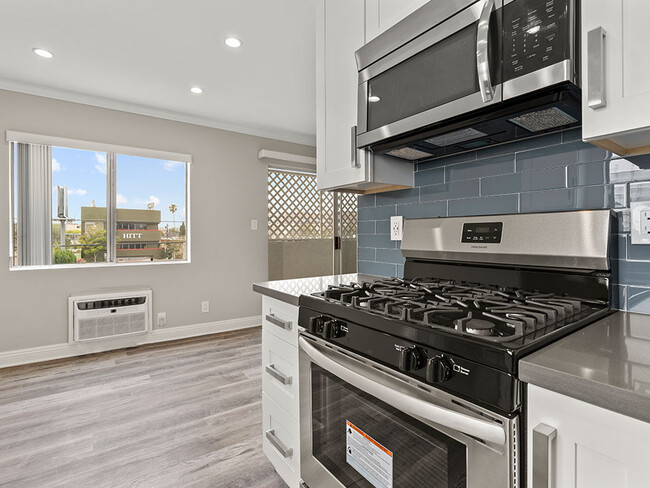 Blue tiled kitchen with stainless steel oven, microwave, and fridge. - Vinton Apartments