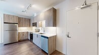 Located on Chapel Street in the heart of New Haven, CT, this two-bedroom, two-bathroom residence offers a thoughtfully designed single-floor layout with modern finishes throughout. The kitchen is a standout feature, showcasing wood-grain cabinetry extending to the ceiling, white quartz countertops, a classic subway tile backsplash, and a full suite of stainless steel appliances including a range, microwave, dishwasher, and refrigerator. Track lighting and warm hardwood-style flooring complete the contemporary aesthetic. Both bathrooms are finished with light wood vanities, white quartz countertops, large mirrors, and walk-in glass-door shower enclosures, maintaining a clean and cohesive design. The bedrooms feature neutral tones, hardwood-style flooring, and tall windows that frame views of the surrounding New Haven cityscape, allowing natural light to fill each room. The primary bedroom offers a generous footprint, while the second bedroom provides a comfortable and equally well-appointed space. A hallway connects the rooms efficiently, contributing to a functional and well-organized floor plan. The overall ambiance is clean, bright, and modern, suited for urban living in one of Connecticut's most vibrant city centers.