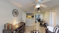 This one-bedroom, one-bathroom apartment is thoughtfully designed to maximize comfort and functionality within a compact, single-story layout. The living area serves as the heart of the home, featuring light wood-style flooring, a ceiling fan with light fixture, and a window that frames a pleasant outdoor view, filling the space with natural light. The open-concept kitchen is separated from the living and dining areas by a peninsula counter with light-colored countertops, providing both a casual breakfast bar and additional prep space. The kitchen is equipped with stainless steel appliances — including a refrigerator, gas range, and microwave — complemented by gray cabinetry and a single-basin sink. A dedicated dining area sits adjacent to the kitchen, offering a natural flow for everyday living and entertaining. The bedroom is a relaxing retreat, highlighted by a ceiling fan, a window with outdoor views, and warm neutral tones that create a calm atmosphere. The bathroom features a tiled tub-shower combination, a gray vanity with white countertop, and a well-lit mirror above the sink. Throughout the unit, consistent neutral tones, light flooring, and ceiling fans in every room contribute to a cohesive, comfortable ambiance.