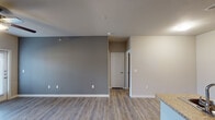 This single-story apartment in Conroe, TX offers a thoughtfully designed layout that balances functionality and modern style. The open-concept living area features wood-look plank flooring, neutral-toned walls with a bold grey accent wall, and a ceiling fan with light fixture. French doors allow natural light to fill the space and provide outdoor access. The galley-style kitchen is a standout feature, boasting dark espresso cabinetry, granite-style countertops, a mosaic tile backsplash, and black appliances including a refrigerator, range, microwave, and dishwasher. A breakfast bar connects the kitchen to the living area. The bedroom is carpeted for comfort and includes a ceiling fan, a window with blinds for natural light, and convenient access to a closet. The bathroom is finished with large-format grey tile surrounding the soaking tub and shower combo, complemented by wood-look flooring, a dark vanity with granite-style countertops, and chrome fixtures. Throughout the unit, clean white baseboards and neutral walls create a cohesive, move-in-ready aesthetic suited for comfortable everyday living.