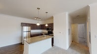 This single-floor residence offers a thoughtfully designed layout that balances comfort and functionality throughout. The kitchen serves as a central highlight, showcasing rich dark cabinetry, granite countertops, and a full suite of stainless steel appliances including a refrigerator, range, and microwave. A peninsula with an integrated sink and pendant lighting overhead creates an inviting space for both meal preparation and casual dining. Crown molding and wood-look flooring add a refined touch to the kitchen and living areas, while the open layout allows the kitchen to flow naturally into the carpeted living room, creating a cohesive and spacious common area. The bedrooms are generously proportioned, each featuring plush carpet, natural light from large windows with blinds, and ceiling fans for year-round comfort. One bedroom includes a walk-in closet, providing ample storage. The bathrooms are well-finished with granite-topped dark vanities, wood-look tile flooring, and tub-shower combinations with chrome fixtures. Clean, neutral wall tones throughout the home create a bright and welcoming ambiance, offering a versatile backdrop ready for personalization.