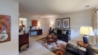This single-floor residence offers a thoughtfully organized layout with distinct living spaces connected seamlessly throughout. The living room serves as the central gathering area, finished with plush carpeting and neutral walls that create a warm, inviting atmosphere. Natural light filters in through windows dressed with roller shades and drape panels, complementing the open, comfortable feel of the space.

The kitchen is efficiently arranged with warm-toned oak cabinetry providing generous storage and a gas range positioned beneath a ventilation hood. Light countertops offer practical workspace, and a full-size refrigerator completes the functional setup.

Adjacent to the kitchen, the dining area accommodates a full dining table and chairs, with a window allowing natural light to brighten the space.

The primary bedroom features carpeted flooring, windows with curtain panels that allow natural light, and a wide double closet offering ample storage. The second bedroom similarly includes carpet, a window with drape panels, and a full-width bi-fold closet for additional storage.

The bathroom is finished with white tile flooring, a vanity with wood cabinetry, a toilet, and a full bathtub with a decorative striped shower curtain, completing the functional and cohesive design of this residence.