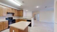 Located at 100 Stonecrest Blvd in Stonecrest, Georgia, this single-floor residence offers a well-designed open-concept layout that seamlessly connects the kitchen and living areas. The kitchen is outfitted with warm honey-toned wood cabinetry, light countertops, a tile backsplash, black appliances including a range and dishwasher, and a central island that provides additional prep and dining space. A peninsula with a built-in sink further enhances the kitchen's functionality. Crown molding and an arched doorway add architectural character to the main living area, which features neutral carpet flooring throughout. The living space also includes a decorative wainscoting accent wall, adding a refined touch. Bedrooms are carpeted and bathed in natural light through large windows that offer pleasant views of surrounding greenery. The bathroom features stone-look tile flooring, a tub-shower combination with white subway tile and a distinctive black decorative tile border, a wood-tone vanity with ample cabinet storage, and a large mirror. A dedicated laundry area with full-size washer and dryer hookups adds everyday convenience. The overall ambiance is clean, functional, and comfortable.