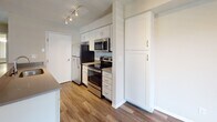 Located along IL-59 in Naperville, IL, this single-floor unit offers a well-designed, open-concept layout that seamlessly connects the kitchen and living areas. The kitchen is equipped with stainless steel appliances — including a refrigerator, electric range, and over-the-range microwave — complemented by white shaker-style cabinetry, light countertops, a tile backsplash, track lighting, and wood-look flooring. A peninsula with a dark countertop and undermount sink bridges the kitchen and living space, providing both functionality and definition between the two areas. The spacious living room features dark hardwood-style flooring and a sliding glass door with vertical blinds that opens to a private patio, allowing generous natural light and outdoor views. A dedicated dining area near the entry offers additional hardwood flooring and a bright window. The bedroom is carpeted and benefits from natural light through a window with blinds. The bathroom includes a single undermount sink with a gray countertop, white cabinetry, a large vanity mirror, and a tub-shower combination. Throughout the unit, textured ceilings, neutral wall tones, and clean finishes contribute to a cohesive and functional living environment.