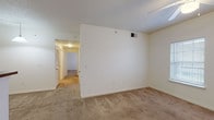 This single-floor space is designed with a practical, functional layout connecting multiple rooms through a central hallway. The bedrooms are carpeted in warm beige tones and each features a ceiling fan with a light fixture, windows fitted with blinds that allow natural light while maintaining privacy, and ample wall space. The primary bedroom includes direct access to a full bathroom and a walk-in closet, providing convenient storage and organization.

The kitchen is outfitted with warm wood cabinetry extending to the upper walls, dark laminate countertops, a double-basin sink, and white appliances including a refrigerator, electric range, and microwave. Light-toned ceramic tile flooring runs throughout the kitchen and utility areas, offering easy maintenance. A pass-through countertop connects the kitchen to the adjacent living area, enhancing the open feel of the space.

Two bathrooms serve the unit; one features a tub-shower combination with a single vanity and mirror, while the second offers a vanity with matching wood cabinetry and dark countertops. Both bathrooms utilize light tile flooring consistent with the kitchen. The overall interior maintains a neutral white and beige palette with textured ceilings throughout.