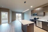 This well-appointed single-story unit offers a thoughtfully designed open-concept layout that seamlessly connects the kitchen and living area. The kitchen serves as a central hub, showcasing dark wood cabinetry extending to the ceiling, crisp white quartz countertops, and a full suite of stainless steel appliances including a range, microwave, dishwasher, and refrigerator. A center island provides additional prep space and casual seating. Linear pendant lighting and recessed fixtures illuminate the kitchen, while light hardwood-style flooring flows throughout the main living areas, enhancing the bright, contemporary atmosphere.

The living area is anchored by a sliding glass door that opens to a private balcony, allowing natural light to fill the space and offering views of the surrounding neighborhood. The bedroom features plush carpet, a ceiling fan, dedicated closet, and windows that bring in additional natural light. The bathroom is well-equipped with an extended wood-toned vanity, white quartz countertop, an illuminated mirror, and a stacked in-unit washer and dryer for added convenience. Neutral tones throughout create a cohesive, modern aesthetic.