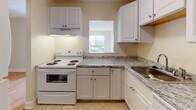 Located at 590 Middle St in Weymouth, Massachusetts, this single-floor residential unit offers a well-designed layout with a clean, neutral aesthetic throughout. Warm hardwood flooring flows seamlessly across the living areas and bedrooms, complemented by cream-toned walls and white trim that lend a bright, cohesive feel to the interior.

The kitchen is thoughtfully appointed with white raised-panel cabinetry, granite-patterned countertops, a stainless steel sink, and a white electric range with an overhead ventilation hood. A pass-through window connects the kitchen to the adjacent living area, enhancing the sense of openness. Natural light filters in through a window above the countertop, providing pleasant outdoor views.

The living room is generously proportioned, featuring hardwood floors, a wall-mounted air conditioning unit, and a sliding glass door that opens to a private balcony overlooking the surrounding area. Additional rooms include well-sized bedrooms, one of which features a built-in closet with louvered bifold doors. Each room benefits from multiple windows that invite natural light.

A standout feature of the unit is the bathroom, which showcases a striking exposed red brick accent wall paired with tile flooring and a white vanity, adding a distinct character to an otherwise clean, modern space.