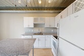 Located in the heart of downtown Ann Arbor at 201 S 1st St, this one-bedroom, one-bathroom unit delivers an urban loft aesthetic across a single floor. The space features light hardwood-style flooring throughout, complemented by exposed metal ductwork and a distinctive industrial ceiling with built-in track lighting that gives the home a modern, loft-inspired character.

The kitchen is a functional standout, offering white cabinetry with frosted glass accents, granite-style countertops, a full suite of white appliances including a range, microwave, and refrigerator, and a deep sink. The open layout connects the kitchen to the living area, maximizing the sense of space.

The living room benefits from floor-to-ceiling windows with bold black frames, filling the room with abundant natural light and offering elevated views of the Ann Arbor downtown skyline. The frosted glass partition wall adds an architectural touch while maintaining an open, airy feel.

The bathroom is thoughtfully designed, featuring a soaking tub with shower, a white vanity with mirror, and warm tile flooring. A stacked washer and dryer unit is conveniently integrated into the bathroom area, adding practical in-unit laundry. Four closets provide generous storage throughout the unit, making efficient use of the compact footprint.