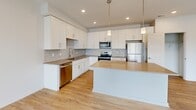 This thoughtfully designed single-floor residence offers a comfortable and modern living experience across a well-utilized layout. The open-concept kitchen and living area serves as the heart of the home, featuring light hardwood flooring that extends throughout the main living spaces. The kitchen is fully equipped with stainless steel appliances, including a refrigerator, range, microwave, and dishwasher. White shaker-style cabinetry with sleek hardware lines the walls, complemented by a subway tile backsplash and warm quartz countertops. A central island provides additional prep space and casual seating, while pendant lighting above adds a refined touch. Recessed lighting illuminates the open living area, which flows seamlessly toward sliding glass doors that open to a private balcony with outdoor views. The bedroom is carpeted for comfort and includes a ceiling fan, a large window that brings in natural light, and convenient closet access. The bathroom features matching white cabinetry, quartz countertops, a single undermount sink, and a full tub/shower combination. Light hardwood flooring continues into the bathroom, tying the space together with a cohesive, clean aesthetic throughout.