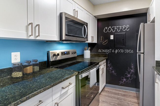 Renovated Package II kitchen with new white cabinetry, granite countertops, stainless steel appliances, painted backsplash, chalkboard accent wall, upgraded lighting and fixtures, and hard surface flooring - AVA Van Ness