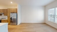 This thoughtfully designed one-bedroom, one-bathroom unit offers a comfortable and functional single-floor layout with clean, modern finishes throughout. The open-concept kitchen serves as the heart of the home, anchored by a generous white quartz island with an undermount sink and matte black faucet, illuminated by stylish pendant lighting. Warm wood cabinetry, a subway tile backsplash, stainless steel appliances — including a French door refrigerator and range — and light hardwood flooring complete the contemporary kitchen aesthetic. The kitchen flows seamlessly into the living area, which is bright and open, extending toward a front entry door with natural light filtering through large windows. The spacious bedroom features plush carpet flooring and a large window overlooking the exterior, providing ample natural light. A dedicated walk-in closet offers dual-level hanging rods and shelving along multiple walls, maximizing storage capacity. The full bathroom is generously sized, featuring wood cabinetry with white quartz countertops, hardwood-style flooring, and ADA-compliant accessibility grab bars. A convenient in-unit washer is also included. The unit presents a clean, neutral palette throughout, creating a bright and welcoming atmosphere.