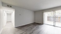 This single-floor unit presents a clean, contemporary aesthetic defined by a consistent palette of crisp white walls, white trim, and grey-toned luxury vinyl plank flooring that runs throughout every room. The open living area is notably bright, benefiting from a full-width sliding glass door fitted with vertical blinds that opens to a private outdoor space, allowing natural light to fill the interior.

The galley-style kitchen is well-appointed with white shaker cabinetry, light quartz countertops, a stainless steel sink with a modern pull-down faucet, and stainless steel appliances including a dishwasher and range. Recessed lighting illuminates the workspace, and a pass-through hallway connects to additional living areas.

The bedrooms are comfortably scaled with neutral walls and windows fitted with horizontal blinds. At least one bedroom features a full-wall sliding closet, providing generous storage. A second room also offers closet access and natural light.

The bathroom is a standout feature, showcasing a soaking tub surrounded by bold, large-format dark marble-effect tiles contrasted with a white marble-patterned tile border. The vanity features white cabinetry with brushed nickel hardware, and the flooring continues the vinyl plank theme. Chrome towel bars and grab bars complete the refined, modern finish.