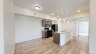 Located in Vineyard, Utah, this well-appointed 2-bedroom, 2-bathroom residence offers a thoughtfully designed single-level floor plan that maximizes functionality and comfort. The open-concept kitchen and living area serves as the heart of the home, featuring light wood-look luxury vinyl plank flooring that flows throughout the main living spaces. The kitchen is equipped with dark wood cabinetry, granite-look countertops, a peninsula with pendant lighting and an integrated sink, and black appliances including a range, microwave, and refrigerator. The living area is bright and airy, with a glass-panel exterior door flanked by sidelight windows that invite an abundance of natural light. Both bedrooms are generously sized, finished with plush wall-to-wall carpeting, and each includes its own dedicated closet with wrap-around hanging rods for ample storage. The two bathrooms mirror each other in design, each offering a tub-shower combination, a wood-toned vanity with granite countertop, a large mirror, and LVP flooring consistent with the rest of the home. Clean white walls and modern brushed-nickel hardware throughout lend the space a fresh, contemporary feel suited for a variety of lifestyles.