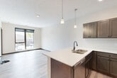 This well-appointed one-bedroom, one-bathroom unit at 410 S 47th St in Lincoln, Nebraska offers a thoughtfully designed layout with modern finishes throughout. The open-concept kitchen serves as the heart of the space, showcasing rich dark-toned cabinetry, crisp white countertops, stainless steel appliances including a refrigerator, range, and microwave, and a peninsula with an integrated sink — ideal for both cooking and casual dining. Pendant lighting and recessed ceiling lights illuminate the kitchen and adjacent living area, which features durable wood-look plank flooring that extends throughout the main living spaces. The bedroom is a comfortable retreat, carpeted for warmth, with large windows that flood the room with natural light and offer views of the surrounding neighborhood. The bathroom is clean and contemporary, featuring a walk-in shower with matte black fixtures, a single vanity with a white countertop, and matching wood-look flooring. A dedicated laundry area with a full-size side-by-side washer and dryer adds everyday convenience. The unit's neutral color palette, dark trim accents, and consistent modern aesthetic create a cohesive and inviting living environment.