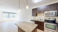 Located at 8250 Westpark Dr, Unit 333 in McLean, Virginia, this one-bedroom, one-bathroom residence offers a well-designed layout across a single floor. Light hardwood flooring runs throughout the main living areas, lending a clean, modern aesthetic and reflecting the abundant natural light that pours in through large windows overlooking lush greenery.

The open-concept kitchen and living room area forms the heart of the unit. The kitchen is appointed with rich, dark-stained cabinetry, granite countertops, a tile backsplash, and a full suite of stainless steel appliances including a refrigerator, range, microwave, and dishwasher. A central island with a granite top and pendant lighting above adds both functional workspace and a stylish focal point.

The living area is spacious and bright, benefiting from a wide window that frames outdoor views and fills the room with natural light. Crisp white walls throughout create a clean, neutral canvas.

The bedroom is a comfortable, well-proportioned space featuring plush carpeting, a large window with outdoor views, and a dedicated closet for storage. The bathroom is finished with tile flooring, a full tub and shower combo with white tile surround, granite-topped vanity, and dark wood cabinetry consistent with the kitchen's design language.