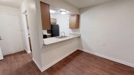 This 1-bedroom, 1-bathroom Mocha Premium unit offers a thoughtfully designed single-floor layout that maximizes both comfort and functionality. The kitchen is a standout feature, showcasing warm honey-toned wood cabinetry that provides ample storage space alongside full-size appliances, including a black refrigerator and range. A light-toned stone-look countertop extends seamlessly into a breakfast bar, creating a convenient pass-through that connects the kitchen to the adjacent living area. This open layout fosters a sense of spaciousness and encourages easy interaction between spaces. The flooring throughout is a rich hardwood-style surface that adds warmth and visual continuity to the unit. Crisp white walls and clean baseboards contribute to a bright, fresh aesthetic that pairs well with the natural tones of the cabinetry and flooring. The overall ambiance of the space is welcoming and move-in ready, blending practical design with a modern, cozy feel. The Mocha Premium designation reflects the elevated finishes and attention to detail that define this thoughtfully appointed home.