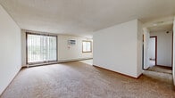 This single-floor unit offers a practical and well-organized layout across three bedrooms, one bathroom, a kitchen, a hallway, and a closet. The open living area is generously sized, featuring wall-to-wall carpet, a textured ceiling, and large vertical-blind-covered sliding glass doors that flood the space with natural light and provide outdoor views. A wall-mounted air conditioning unit and baseboard heating ensure year-round comfort.

The kitchen is equipped with warm oak cabinetry, a full suite of white appliances including a range, over-the-range microwave, and refrigerator, along with laminate countertops and easy-care tile flooring. A peninsula provides additional counter space and separates the kitchen from the rest of the unit.

The primary bedroom is notably spacious, featuring a dedicated closet with built-in shelving and warm wood-trimmed doors. Each bedroom includes plush carpeting, baseboard heating, and wood-framed windows that bring in ample natural light.

The bathroom features a single-sink vanity with oak cabinetry, a tiled tub-shower combination, and neutral, easy-to-maintain finishes throughout. Clean white walls and warm wood trim details tie the entire unit together, creating a cohesive and functional living environment.