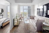 Located at 125-133 Bronte Road in Oakville, Ontario, this two-bedroom, one-bathroom unit offers a well-designed, single-level layout with a contemporary aesthetic throughout. Light-toned hardwood flooring and a neutral white palette create a clean, cohesive look that enhances the sense of openness across the floor plan.

The kitchen is outfitted with two-tone grey cabinetry extending to the ceiling, dark quartz countertops, stainless steel appliances including a full-size refrigerator, electric range, built-in dishwasher, and microwave. A central island with a dark countertop provides additional prep space and connects seamlessly to the open-concept living area.

The living room is bright and airy, benefiting from large floor-to-ceiling windows and access to a balcony with views of the surrounding Oakville neighbourhood and treetops. The primary bedroom continues the floor-to-ceiling window design, filling the room with natural light, and includes a walk-in closet with built-in shelving. The second bedroom also offers closet storage. The bathroom features a full soaker tub with clean white subway tile surround. Throughout, the unit maintains a modern, minimalist character with thoughtful use of space.