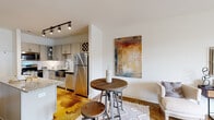 Located at 1200 Isner Ln in Garner, North Carolina, this single-floor residence combines contemporary finishes with a warm, inviting ambiance throughout. The kitchen is a standout feature, outfitted with gray shaker-style cabinetry, granite countertops, a stainless steel farmhouse sink, white subway tile backsplash, and a full suite of stainless steel appliances including a refrigerator, range, microwave, and dishwasher. A kitchen island provides additional prep and dining space, complemented by a compact dining area nearby. Distinctive stained concrete floors in a rich amber tone flow throughout the living areas, adding a unique industrial-chic character to the space. The living room is bright and open, featuring large windows with plantation-style shutters and a glass-paneled entry door that opens directly to the outdoors, filling the room with natural light and views of the surrounding community. The bedroom is generously sized, offering dual windows, a ceiling fan, and ample natural light. It is accompanied by a walk-in closet with multi-tier wire shelving for organized storage. The bathroom includes a walk-in shower with built-in shelving. The overall design balances modern practicality with comfortable, livable style throughout.