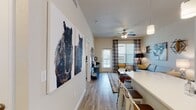 This well-designed single-floor residence offers a seamless open-concept layout that connects the kitchen, dining, and living areas into one cohesive and functional space. The kitchen is a standout feature, showcasing crisp white shaker cabinetry, quartz countertops, a subway tile backsplash, stainless steel appliances including a refrigerator, range, and microwave, and a generous island with bar seating — ideal for casual dining and entertaining. Track and pendant lighting accentuate the clean, modern aesthetic throughout the kitchen.

The living area is bright and welcoming, filled with natural light from large windows dressed with plaid curtains and a sliding glass door providing outdoor access. Wood-look flooring runs throughout the main living spaces, while a ceiling fan adds comfort overhead.

Two bedrooms offer comfortable retreats, each featuring plush carpeting, generous windows with sheer curtains, and ceiling fans. The primary bedroom connects directly to an en-suite bathroom appointed with dual white vanities, quartz countertops, large mirrors, and direct access to a spacious walk-in closet with built-in shelving.

The overall ambiance is contemporary and inviting, with a neutral color palette, modern fixtures, and thoughtful design details that make this space both functional and visually appealing.