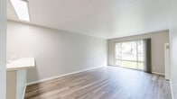 Located at 801 14th St in Oakland, CA, this two-bedroom, single-floor residence offers a practical and comfortable layout. The interior is finished with light wood-style vinyl flooring throughout, neutral gray-toned walls, and textured ceilings, creating a clean and cohesive aesthetic.

The combined kitchen and living room serves as the heart of the unit. The kitchen features warm oak cabinetry, a white tile-style countertop with a peninsula that includes a stainless steel sink, a full-size refrigerator, and an electric range. The living area is open and bright, highlighted by a large sliding glass door that invites natural light and provides views of the surrounding greenery.

Both bedrooms are well-sized, with the primary bedroom offering a generous footprint. Each room benefits from natural light through individual windows and is serviced by a dedicated closet — both fitted with sliding doors and built-in hanging rods for organized storage. Wall-mounted heating units are present in the living and bedroom areas.

A hallway connects the main living spaces to the bedrooms, maintaining a logical and efficient floor plan. The overall ambiance is clean, neutral, and move-in ready, making it a functional residential space in the heart of Oakland.