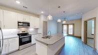 This thoughtfully designed one-bedroom, one-bathroom unit in Grand Prairie, Texas, offers an efficient and modern single-floor layout. The open-concept kitchen serves as the heart of the space, featuring white shaker cabinetry, a subway tile backsplash, granite countertops, and a large center island with a built-in sink. Stainless steel appliances, including a French door refrigerator, electric range, and built-in microwave, complement the contemporary aesthetic. Pendant lighting and recessed fixtures illuminate the kitchen, which flows naturally into the living area. Wood-style flooring runs throughout the main living areas, adding warmth and cohesion. The bedroom is carpeted and includes a ceiling fan, a window with natural light, and direct access to the bathroom. The full bathroom features granite countertops, dual sinks, white cabinetry, wood-style flooring, and a bathtub-shower combination. A dedicated closet provides storage convenience. French doors lead to a private outdoor area enclosed by a metal fence with a manicured lawn—ideal for relaxing outdoors. The exterior entry features a covered porch, providing a welcoming transition into the unit.