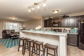 This two-floor space is thoughtfully designed with a cohesive, modern aesthetic that balances functionality and comfort. The open-concept main living area seamlessly connects the kitchen, dining, and living spaces, creating an inviting and social environment. The kitchen is outfitted with dark espresso cabinetry reaching to the ceiling, black appliances including a range, microwave, and refrigerator, and a central island with bar seating — ideal for casual dining and entertaining. Light wood-style flooring runs throughout the main living areas, complementing the warm neutral wall tones.

The living room is generously sized, accommodating a large sectional sofa and entertainment setup, and benefits from natural light through multiple windows. A front entry door with a sidelight window adds to the brightness of this area.

The bedrooms are carpeted and well-proportioned, each featuring large windows that bring in natural outdoor views. The rooms provide ample space for a full bedroom suite and a dedicated study or workspace area.

The bathrooms are finished with tile flooring and dark vanity cabinetry. One bathroom features a tub-shower combination, while another includes a single-sink vanity with a large mirror. Both maintain a clean, consistent design language that ties the overall space together.