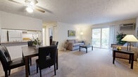 This 1-bedroom, 1-bathroom unit is thoughtfully designed to maximize its compact footprint across a single floor. The open living and dining area serves as the heart of the space, featuring plush wall-to-wall carpeting, a textured ceiling, and a ceiling fan. A charming exposed brick accent wall adds character near the entryway, while large sliding glass doors flood the room with natural light and provide direct access to a private outdoor balcony. The kitchen is efficiently laid out and connects seamlessly to the dining area. The bedroom is a comfortable retreat with carpeted floors, a ceiling light fixture, a baseboard heating unit, and a window dressed with sheer curtains that allow soft natural light. A closet provides convenient storage within the room, with direct access to the full bathroom. The bathroom is clean and bright, featuring a tiled tub-shower combination, mosaic tile flooring, and a vanity with a white countertop. Throughout the unit, neutral tones and warm lighting create a calm, inviting ambiance suited to everyday living.