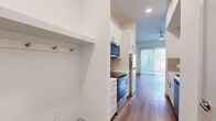 Located at 3900 PGA Pkwy in Frisco, TX, this efficiently designed studio offers a thoughtful layout across a single floor, making excellent use of every square foot. Warm wood-style plank flooring flows continuously throughout the space, creating a cohesive and inviting atmosphere.

The combined kitchen and living area serves as the heart of the unit. The kitchen is outfitted with white shaker-style cabinetry featuring brushed nickel hardware, stainless steel appliances including a refrigerator, electric range, and over-the-range microwave, and light countertops that complement the clean, modern aesthetic. A built-in nook near the entry provides a convenient coat and bag storage area. A ceiling fan overhead adds both comfort and style to the living space.

A full-width sliding glass door with vertical blinds fills the living area with natural light and opens to a private outdoor space with green landscaping, offering a welcome connection to the outdoors. The open layout provides flexibility for furniture arrangement.

The bathroom is clean and contemporary, featuring white cabinetry with brushed nickel pulls, a single-basin vanity with white countertop, a large mirror, and a towel bar. The same warm wood-style flooring extends into the bathroom, maintaining design consistency throughout the unit.