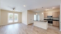 Located at 2700 East McKinney Street in Denton, TX, this thoughtfully designed one-bedroom, two-bathroom residence offers a cohesive open-concept floor plan finished with light wood-look flooring throughout. The living area is bright and airy, featuring a ceiling fan and a glass door that invites natural light while providing outdoor access. The kitchen is a functional centerpiece of the home, showcasing dark granite countertops, a peninsula island with pendant lighting, light-toned cabinetry, stainless steel appliances including a refrigerator, range, and microwave, and a double-basin sink. A hallway connects the main living areas to the private quarters, maintaining a clean and organized flow. The generously sized primary bedroom receives abundant natural light through multiple windows with blinds and features a ceiling fan and direct access to a dedicated closet. The bathrooms are well-appointed, with one featuring a double-sink vanity with dark granite countertops and a tiled tub-shower combination. Additional storage is provided by a closet accessible from the main living space. Neutral warm tones on the walls and clean white trim complete the polished, move-in-ready aesthetic of this Denton residence.
