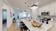 This thoughtfully designed 2-bedroom, 2-bathroom residence offers a comfortable and modern living experience across a single floor. The open-concept layout seamlessly connects the kitchen and living room, creating a spacious and sociable atmosphere bathed in natural light from multiple windows.

The kitchen is a standout feature, showcasing a large granite-topped island with bar seating, illuminated by striking matte black pendant lights. White shaker cabinetry, a subway tile backsplash, and a full suite of stainless steel appliances — including a refrigerator, range, and built-in microwave — complete this functional and stylish space. Light wood-tone flooring flows throughout the main living areas.

The living room is bright and welcoming, with vaulted ceilings, a ceiling fan, and large windows that fill the room with natural light. A wall-mounted electric fireplace serves as a focal point alongside the TV.

The primary bedroom offers generous proportions, plush carpeting, a ceiling fan, and a softly lit, tranquil atmosphere. The second bedroom is equally comfortable, featuring the same warm, neutral palette. Both bathrooms are clean and well-finished, with one featuring a full soaking tub and tiled surround. Two closets and a dedicated hallway provide practical storage throughout.