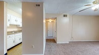 This single-floor 1-bedroom, 1-bathroom unit offers a practical and comfortable layout designed to maximize everyday livability. The living room is generously sized, featuring soft wall-to-wall carpeting, a ceiling fan with light fixture, and a sliding glass door dressed with vertical blinds that invites natural light and provides access to the outdoors. A hallway connects the main living area to the rest of the unit, lined with white doors and lit by a ceiling-mounted fixture for a clean, welcoming feel. The kitchen is laid out in a galley style, with white cabinetry on both sides, dark laminate countertops, a stainless steel sink, a dishwasher, a gas range, and a full-size refrigerator — all set atop warm wood-look vinyl flooring. The bedroom is a quiet, carpeted retreat with a window that allows natural light to filter in, complemented by a textured ceiling. The bathroom features a wide white vanity with ample cabinet storage, a dark countertop, a single basin sink, a mirrored medicine cabinet, and wood-look flooring. Throughout the unit, neutral warm-toned walls, textured ceilings, and consistent finishes create a cohesive and move-in ready living environment.